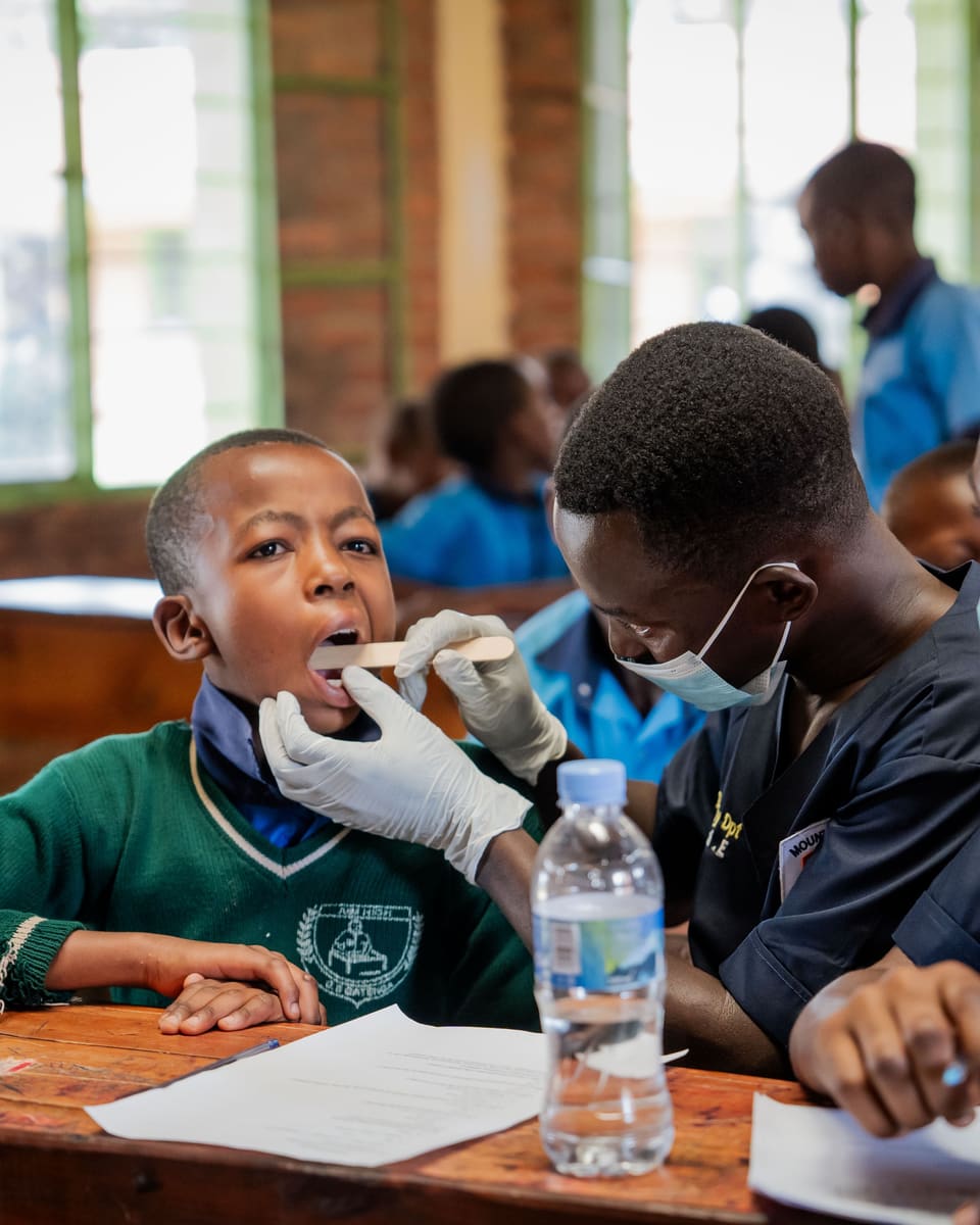 A volunteer dentist in gloves checks a schoolboy's teeth at a classroom desk during a free screening